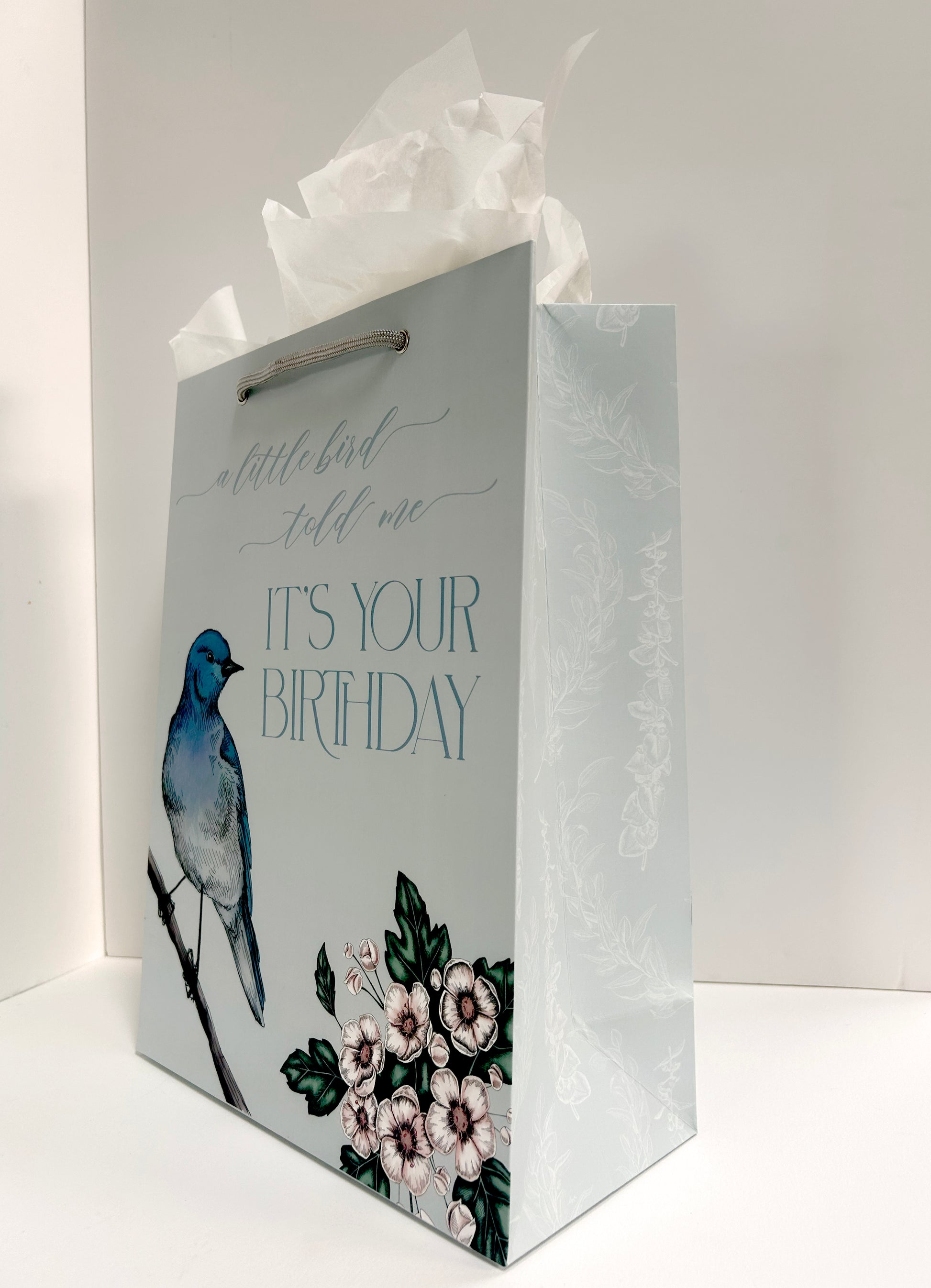 Standing up, angled photo of blue gift bag with florals that reads "A little bird told me it's your birthday" by Rust Belt Love