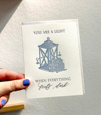 Letterpress love card with a lantern and florals that says " You Are A Light When Everything Feels Dark" By Rust Belt Love