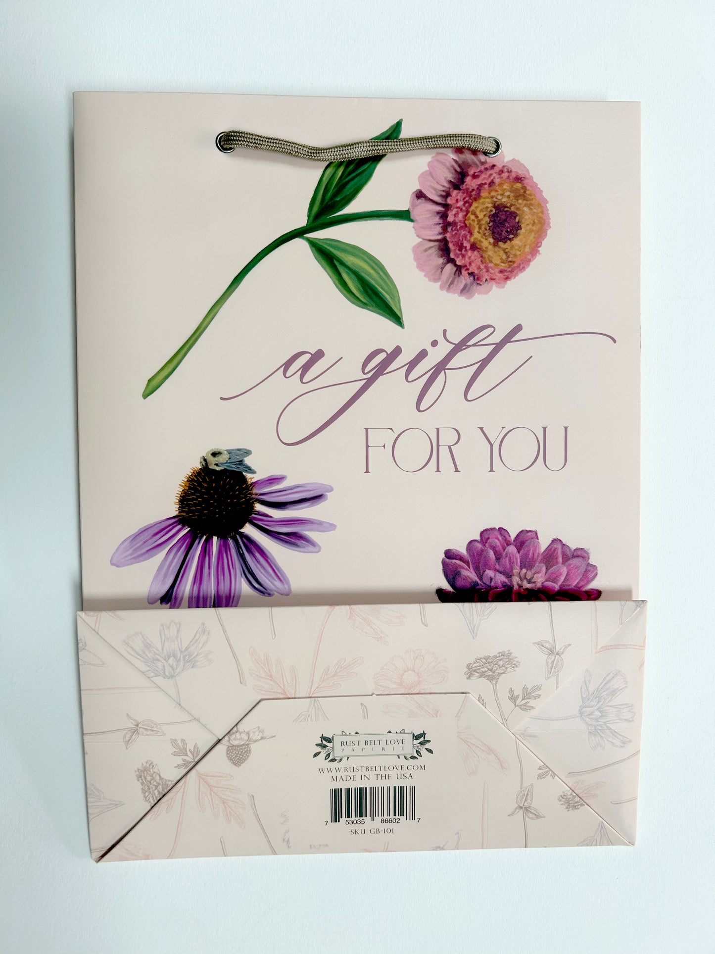Flatlay picture of Rust Belt Love's pink gift bag with florals on it that reads "A gift for you", with the bottom of the bag showing