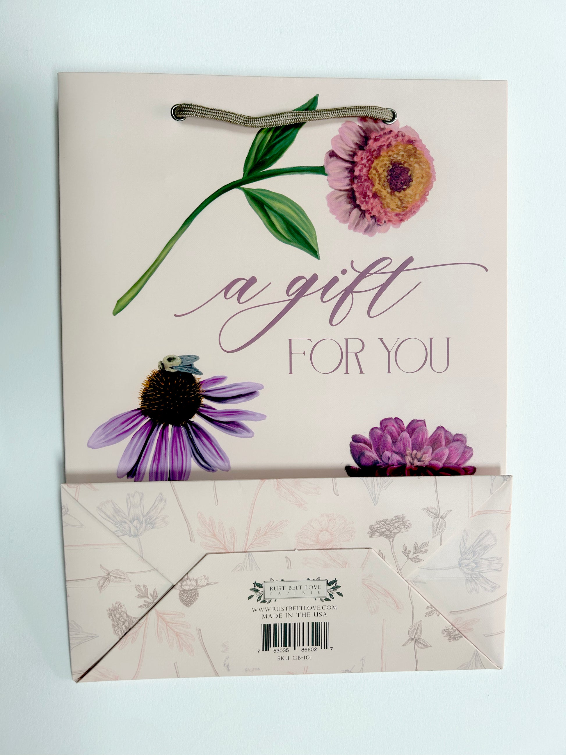 Flatlay picture of Rust Belt Love's pink gift bag with florals on it that reads "A gift for you", with the bottom of the bag showing
