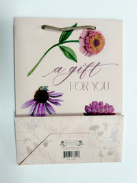 Flatlay picture of Rust Belt Love's pink gift bag with florals on it that reads "A gift for you", with the bottom of the bag showing