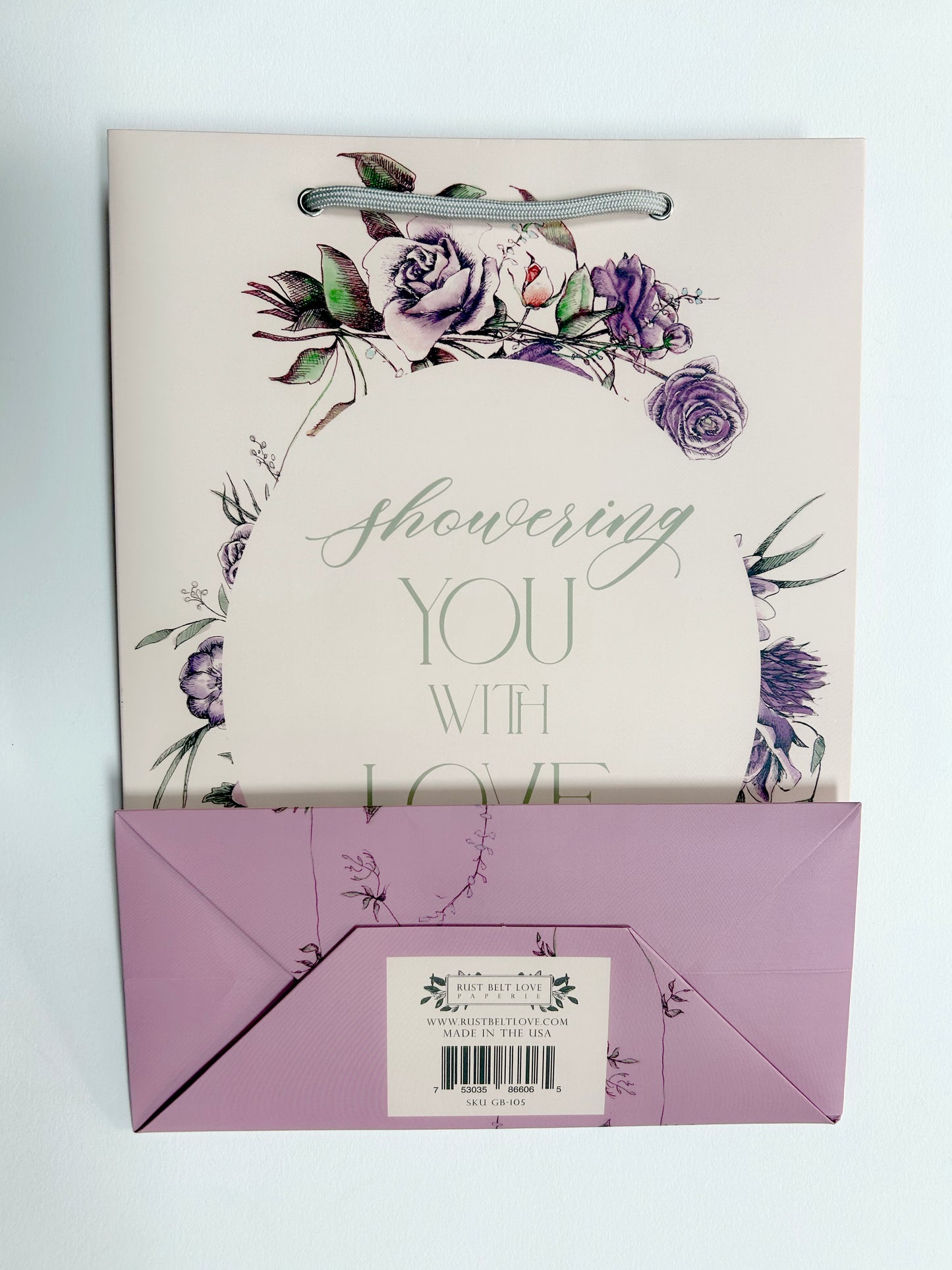 Flat pink floral gift bag that reads "Showering you with love" by Rust Belt Love, that shows the bottom of the bag with barcode