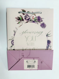 Flat pink floral gift bag that reads "Showering you with love" by Rust Belt Love, that shows the bottom of the bag with barcode