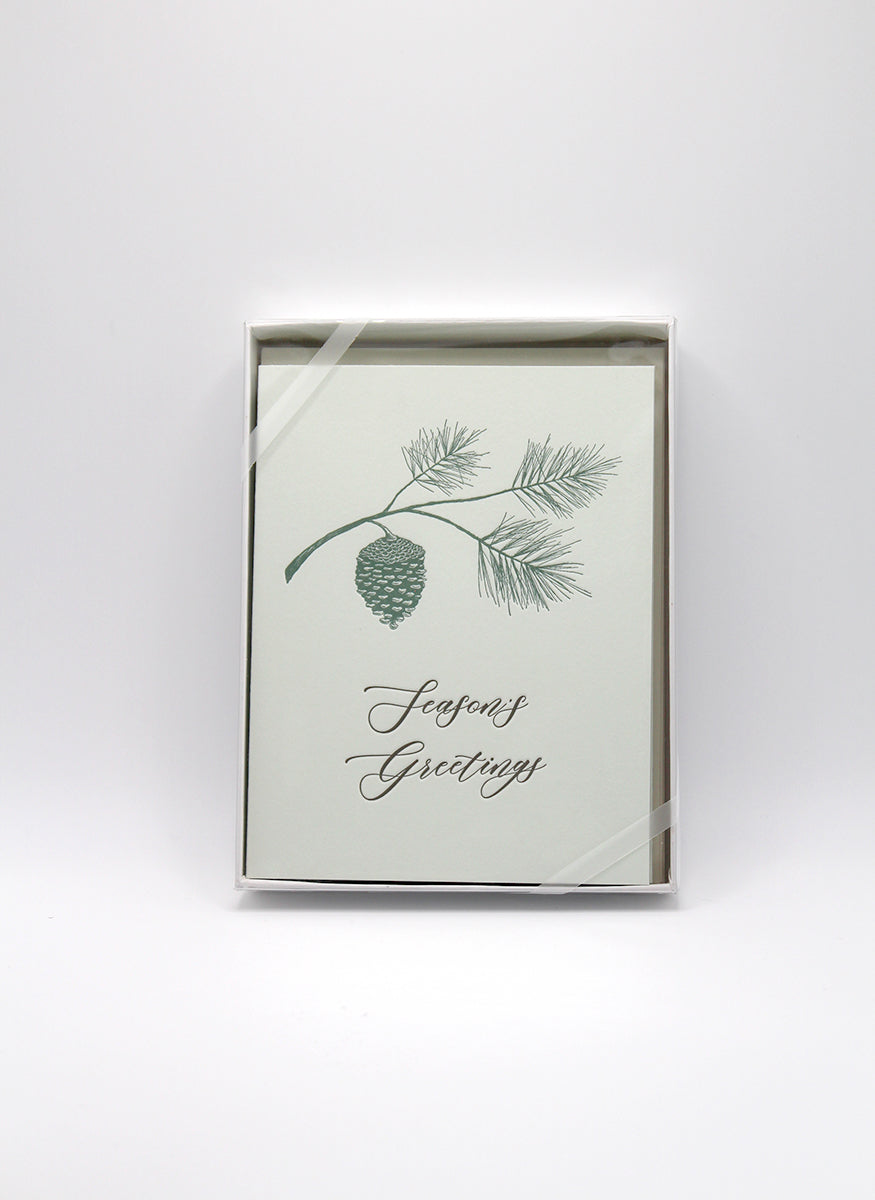 Box of green letterpress holiday cards with branch and pinecone that reads "Season's Greetings" by Rust Belt Love