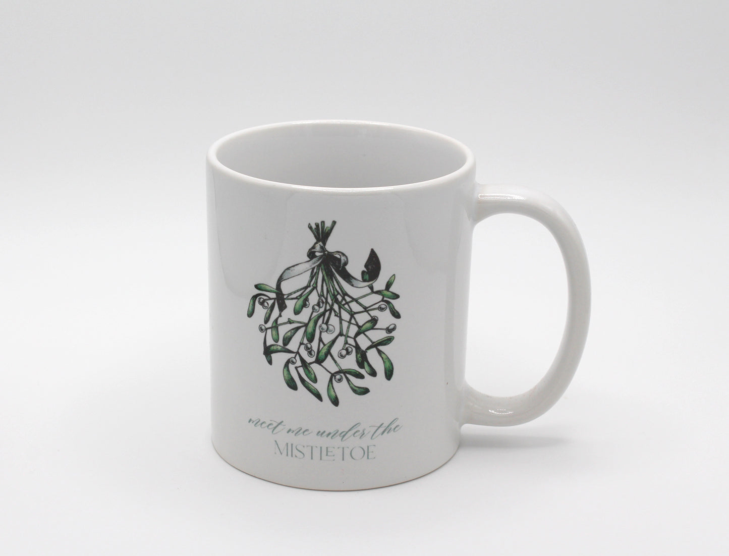 White ceramic mug with a mistletoe that says "meet me under the mistletoe by Rust Belt Love 