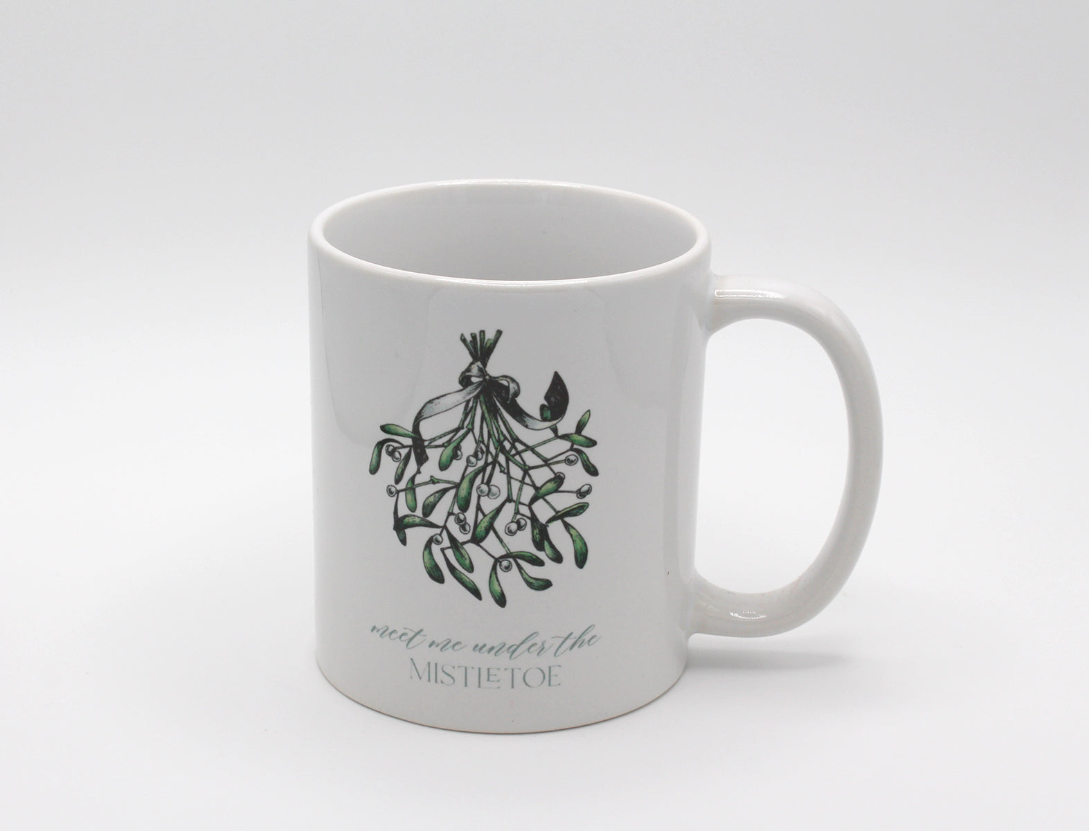 White ceramic mug with a mistletoe that says "meet me under the mistletoe by Rust Belt Love 
